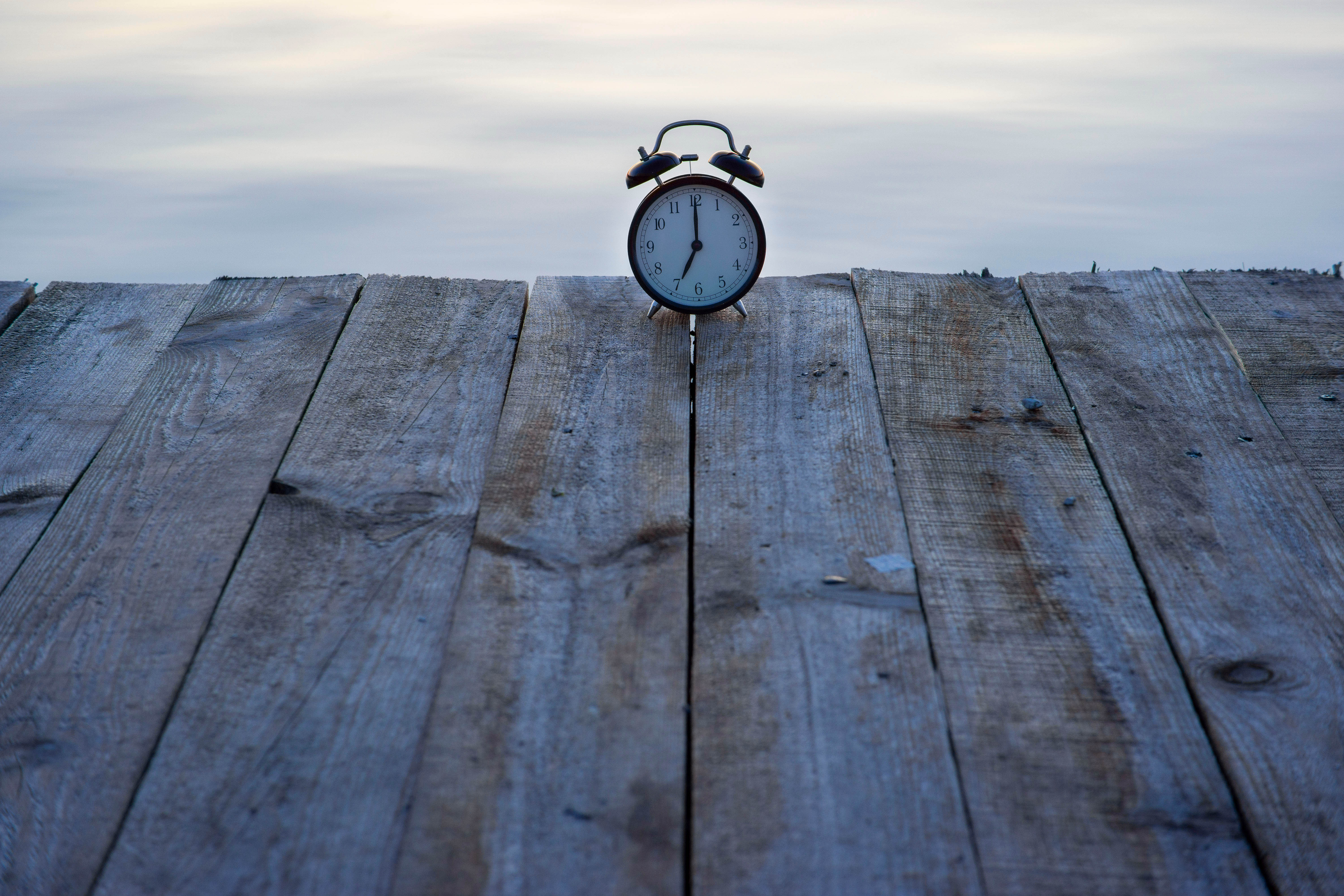 An old alarm clock sits at the edge of a dock with water beyond